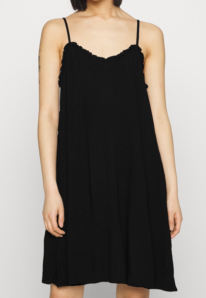 Černé šaty bez rukávů s volným střihem, s volánkovým výstřihem a tenkými ramínky. Materiál vypadá lehký a strukturovaný.