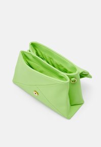 Grön väska i konstläder med triangulär form, utrustad med två fack, texturerad yta och ett guldtonat knappstängning.