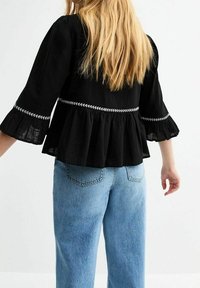 Top peplum negro con mangas acampanadas, decorado con bordado blanco en la cintura. Combinado con pantalones vaqueros de tiro alto en azul claro.