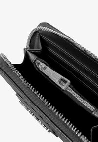 Interno di un portafoglio in pelle nera con zip argentata, numerosi scomparti per carte e un tirazip con marchio. Superficie texturizzata e design pulito.