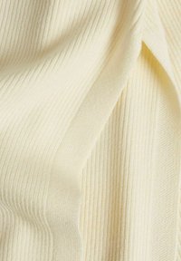 Nahaufnahme von weichem, cremefarbenem Rippstoff mit Falten, die die Textur und das Strickmuster hervorheben.