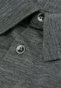 Grijze polo shirt stof met een gestructureerd oppervlak, voorzien van een kraag en twee ronde knopen nabij de hals.