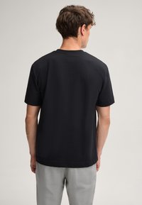 Zwart katoenen T-shirt met ronde hals en korte mouwen, met een eenvoudig ontwerp en een losse pasvorm. De achterkant toont een bescheiden lengte en stiksel details.