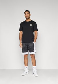 Svart t-skjorte med gull-logo, kombinert med grå mesh-shorts med hvit kant. Fullført med hvite joggesko og sporty sokker.