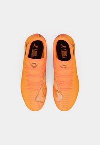 Pomarańczowe buty piłkarskie o gładkiej teksturze, z gradientowym wzorem na przodzie, płaskimi sznurowadłami i nadrukowanym logo na języku.