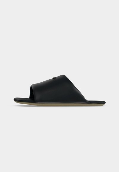 Sandale noire en cuir à bout ouvert avec une large bride et une semelle beige plate, vue de profil sur un fond gris clair.