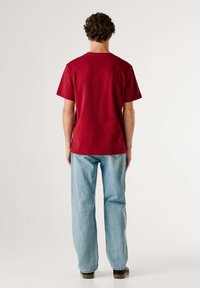 Rood katoenen T-shirt met korte mouwen, ronde hals en een losse pasvorm, gecombineerd met lichtblauwe spijkerbroek en zwarte schoenen.