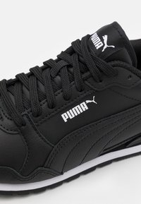 Černá sportovní bota s vrchní částí z syntetické kůže, texturovaným povrchem, polstrovaným jazykem, šněrováním a bílým logem. Gumová podrážka pro lepší přilnavost.