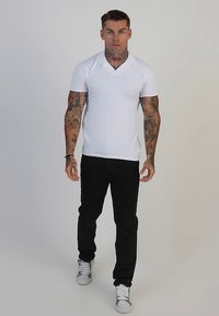 Polo blanc à manches courtes avec col en V, associé à un pantalon noir et des baskets blanches. Tissu lisse et coupe ajustée.