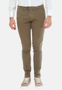 Chinos verde oliva con un design slim fit, realizzati in tessuto misto cotone, dotati di tasche frontali e sneakers marroni con lacci bianchi.