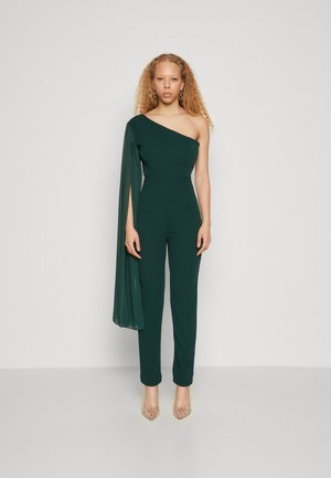 Salopetă verde cu un umăr, cu un mânecă fluidă, picioare conice și material neted. Purtați cu tocuri ascuțite, decorate.