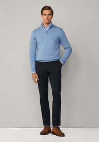 Jasnoniebieski, lekki sweter z rozpinanym kołnierzem, w połączeniu z ciemnymi spodniami i brązowymi butami na sznurówki. Gładka faktura, swobodny styl.