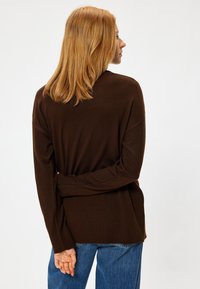Suéter de punto marrón con mangas largas y corte relajado, con un dobladillo y puños con ribete. Combinado con jeans de tiro alto en azul claro.