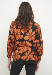 Blusa nera con grande motivo floreale arancione, dotata di maniche lunghe con polsini arricciati e tessuto liscio e leggero.