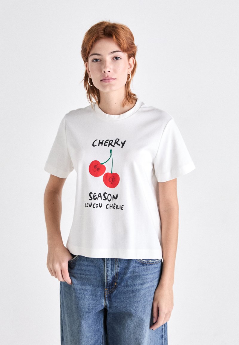 Weißes Baumwoll-T-Shirt mit rotem Kirschgrafikdruck und dem Text "CHERRY SEASON coucou chérie", kurzen Ärmeln und lockerer Passform.