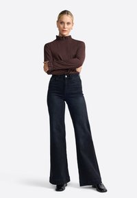 Brown long-sleeve top with a ruffled collar, paired with high-waisted, wide-leg black jeans and black shoes. Simple and tailored design.