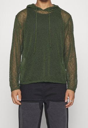 Groene, doorzichtige gebreide hoodie met een gestructureerde afwerking, trekkoorden bij de nek en lange mouwen, gecombineerd met donkere broeken.