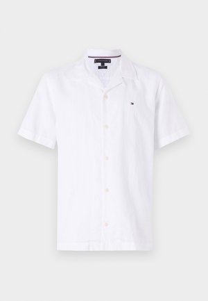 Chemise blanche à manches courtes en lin, dotée d'un col en V, de boutons sur le devant et d'un petit logo de marque sur la poitrine gauche.