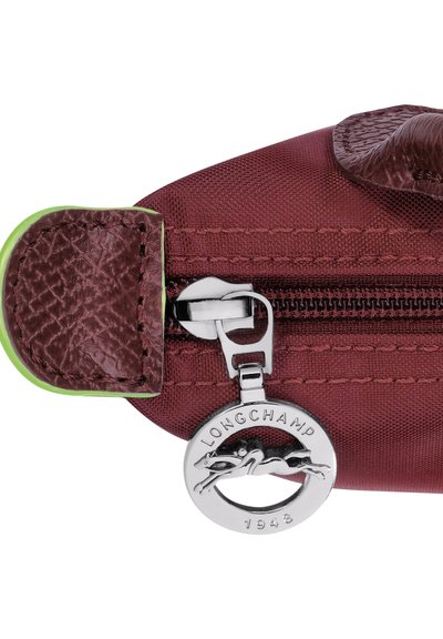 Burgundisches Nylonetui mit einem genoppten braunen Lederumschlag, silbernem Reißverschluss mit einem Longchamp-Logo-Anhänger und einem grünen Akzenttab.