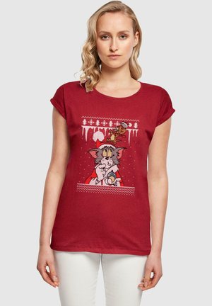 Rotes T-Shirt mit kurzen Ärmeln, das einen Druck von cartoonähnlichen Charakteren mit weihnachtlichem Thema zeigt, vor einem Design mit schneebedecktem Hintergrund.