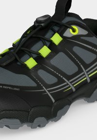 Chaussure de randonnée gris foncé et noire avec des accents vert néon, lacets à tirage rapide et semelle texturée et robuste.