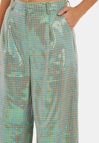 Losse broek in een gemusterde stof met een mix van iriserende pailletten en ruitjes in blauwe, groene en bruine tinten.