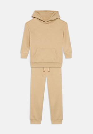 Sudadera beige con capucha, bolsillo canguro en la parte delantera y pantalones jogger a juego, con cinturilla ajustable y tobillos acampanados.