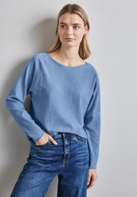 Maglione azzurro chiaro a maniche lunghe con vestibilità morbida e scollatura ampia, abbinato a jeans blu scuro. Texture liscia e design casual.