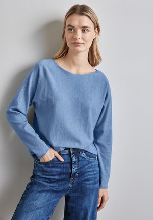 Pull bleu clair à manches longues, avec une coupe décontractée et un col large, associé à un jean bleu foncé. Texture lisse et design décontracté.