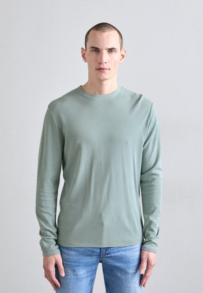 Chemise à manches longues vert clair avec un col rond, fabriquée en tissu doux. Associée à un jean en denim bleu, avec un design simple et ajusté.
