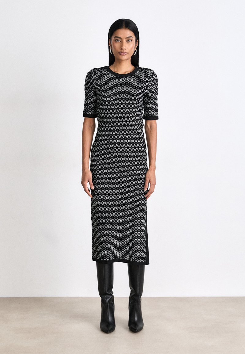 Black-and-white patterned knitted dress with short sleeves and a round neck, paired with black knee-high boots. Smooth texture, fitted shape.