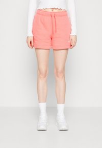 Růžové fleecové šortky s elastickým pasem, šňůrkou a bočními kapsami. Mají hladkou texturu a malou logovou akcentaci na přední straně.