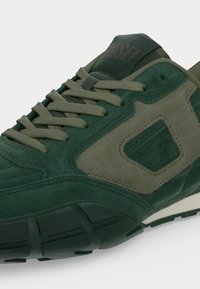 Baskets en daim vert foncé et olive avec lacets et une semelle épaisse texturée, montrant les détails latéraux et les coutures sur la tige.