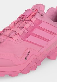 Κοντινό πλάνο ροζ παπουτσιού για trail running Gore-Tex με υφή στο πάνω μέρος, ενισχυμένες πλευρές και ελαστικά κορδόνια με μηχανισμό κλειδώματος.