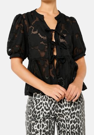 Woman wearing black sheer floral blouse with tied bows and puff sleeves, paired with high-waist black and white leopard print jeans.