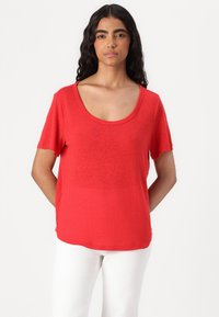 T-shirt rosso a maniche corte con scollo rotondo, realizzato in tessuto leggero. Vestibilità leggermente rilassata, abbinato a pantaloni bianchi.