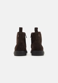 Botine ankel din suede maro au un finisaj neted, închidere cu fermoar, cusături tonale și talpă din cauciuc cu branding la călcâi.