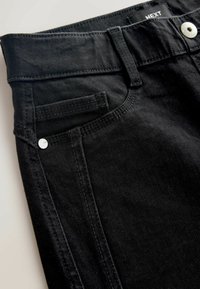 A fekete farmernadrág öt zsebbel rendelkezik, kontrasztos varrással, elöl gombos záródással és ezüst színű kiegészítőkkel.