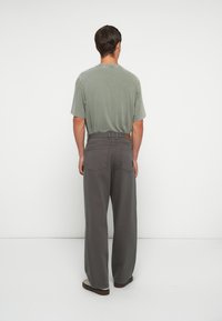 Gray wide-leg pants with back pockets, paired with a faded green short-sleeve shirt, viewed from the back against a white background.