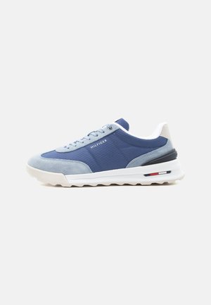 Blå og grå lav sneakers med hvid sål, snørelukning og teksten "Hilfiger" på siden.