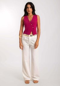 Top sin mangas en color fucsia con escote en V y tres botones decorativos, combinado con pantalones de lino blancos de pierna ancha y sandalias sencillas.
