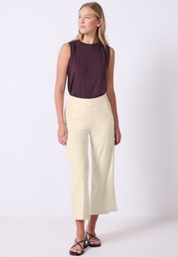 Mouwloze donker paarse top gecombineerd met lichte crèmekleurige wijde broek met zijzakken en een platte tailleband. Zwarte sandalen met bandjes.