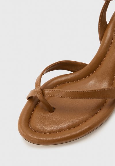 Καφέ δερμάτινο σανδάλι με θηλιά για το δάχτυλο και λεπτό λουράκι που διασχίζει το πόδι, με εμφανή ραφή στην άκρη της σόλας.