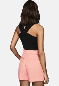 Top negro sin mangas con tirantes cruzados en la parte posterior, combinado con pantalones cortos rosa de talle alto con una tela texturizada y bolsillos laterales.