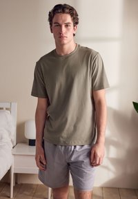 T-shirt en coton vert olive avec col rond, associé à un short gris clair. Texture douce, coupe décontractée et manches courtes.