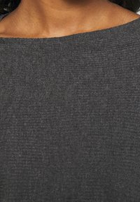 Dunkelgrau gestricktes Oberteil mit weitem Ausschnitt und einem weichen, strukturierten Stoff mit einem subtilen Muster. Nahaufnahme des Materials.