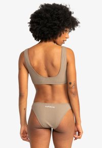 Brown ribbed bikini set featuring a scooped back top with wide straps and low-rise bottoms. Subtle branding on the rear. Smooth texture.