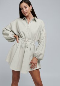 Lichtgrijze jurk met een col-kraag, lange pofmouwen en een elastische taille, met een vloeiende A-lijn rok.