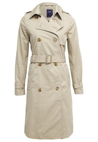 Trench-coat beige croisé avec ceinture, épaulettes, poignets à boutons et poches avant de la marque GAP.