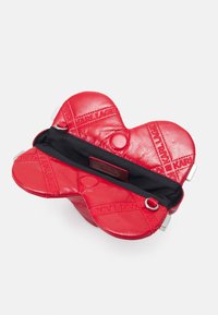 Sac à main en forme de cœur rouge, fabriqué en cuir texturé. Présente un intérieur noir, des accessoires en métal argenté et des détails de marque en relief. Design ouvert.